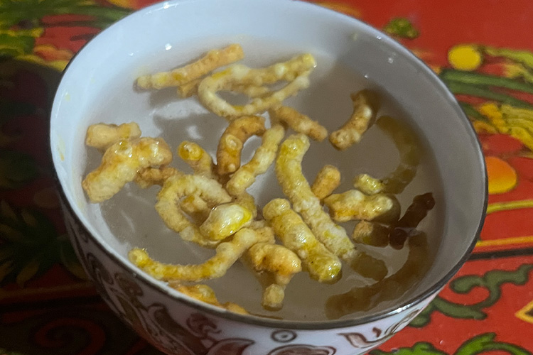 Local alcohol being served in ceramic cup with fried churpi/Himalayan cheese. It is a local Tsum valley's drink.