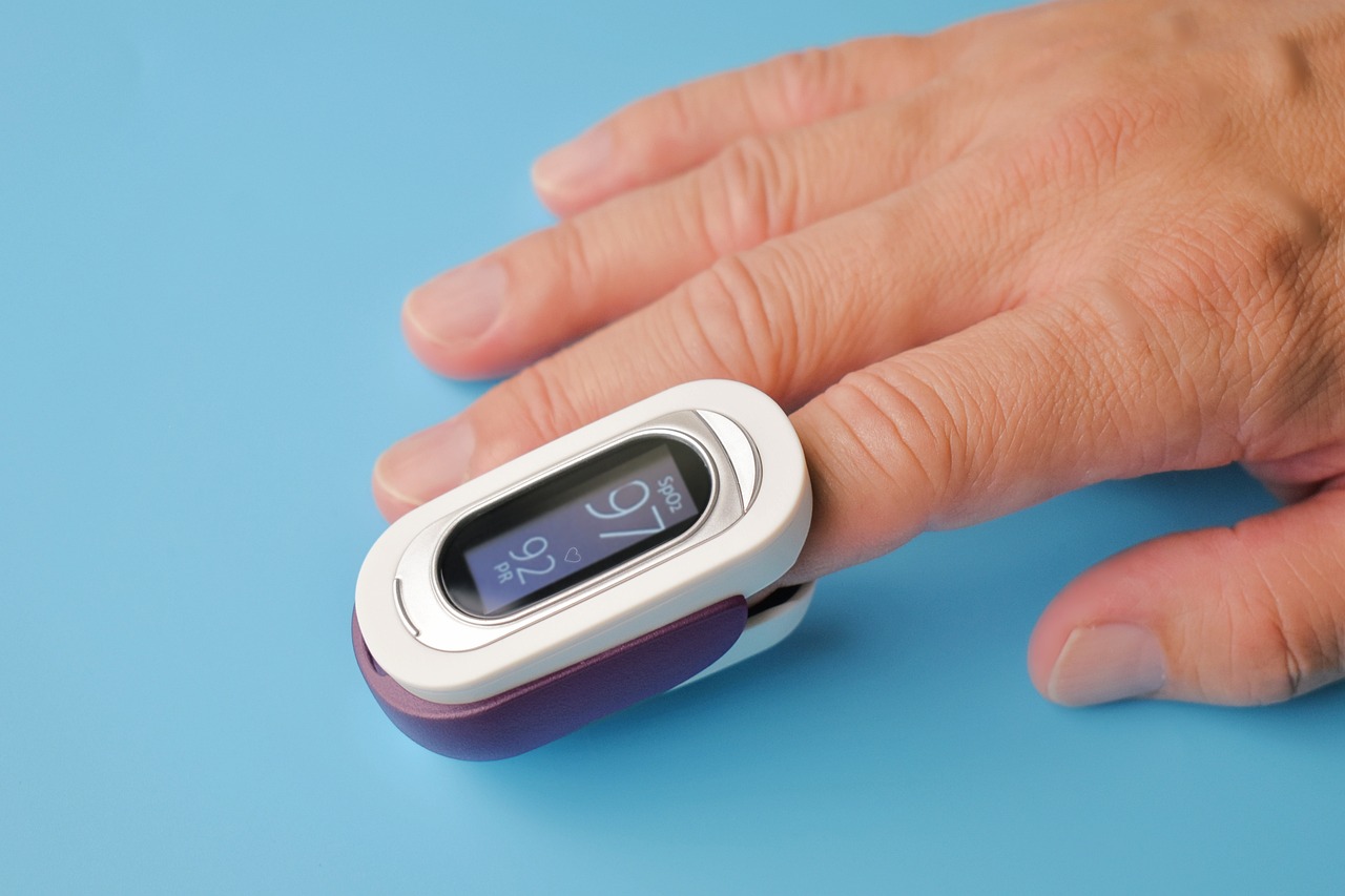 a white person male hand is shown with the index finger inside a white and purple oximeter.